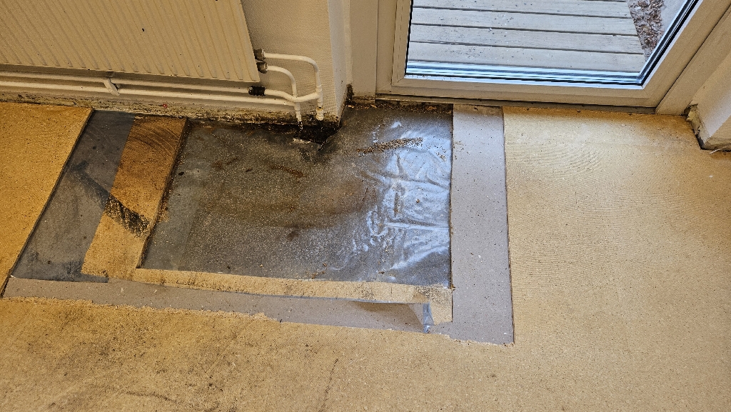 Frilagd golvkonstruktion vid radiator efter rivning av golvmatta, vattenskada i Barkarby